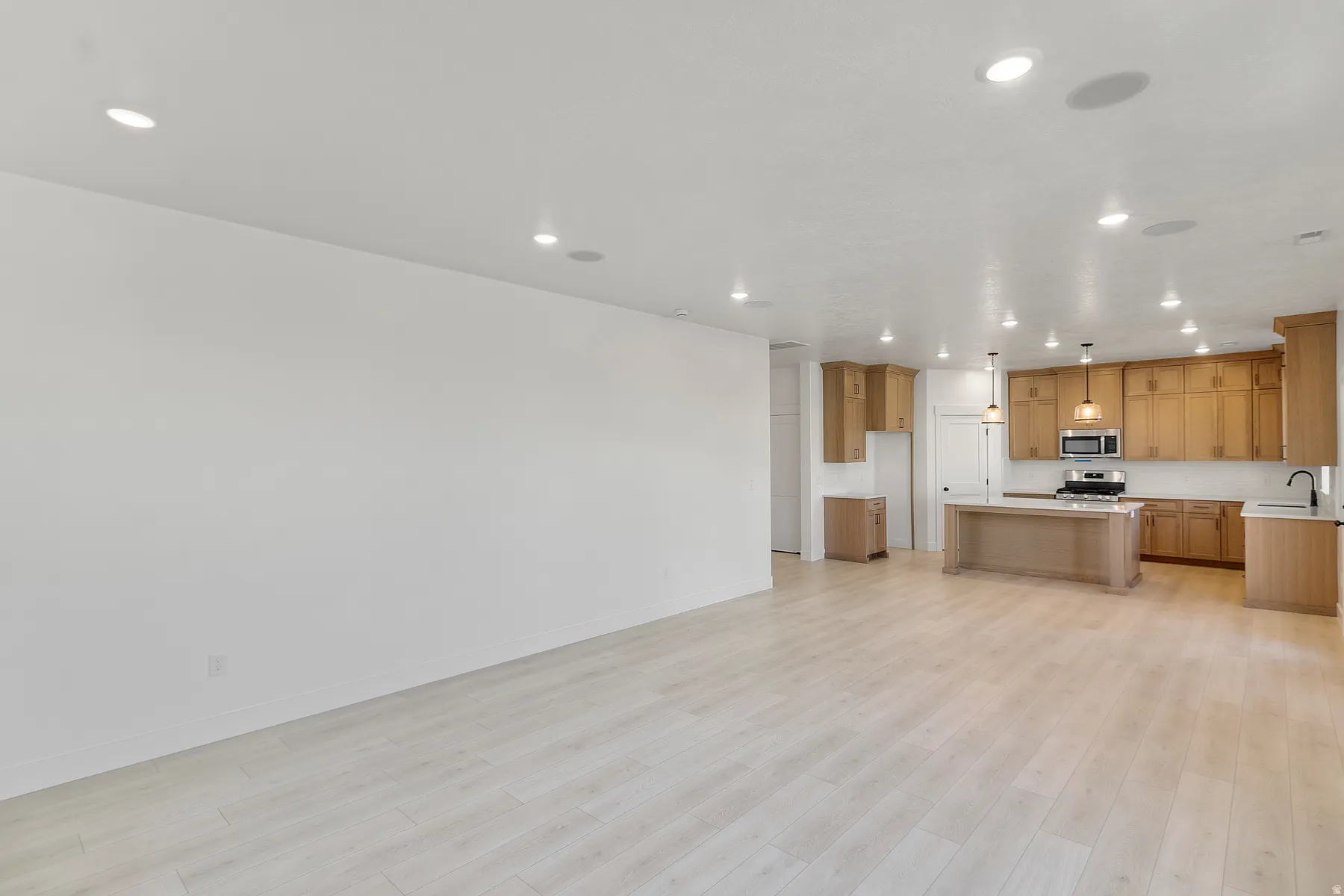 Open-concept living space featuring wood-finish flooring, recessed lighting, and a kitchen with light wood cabinetry