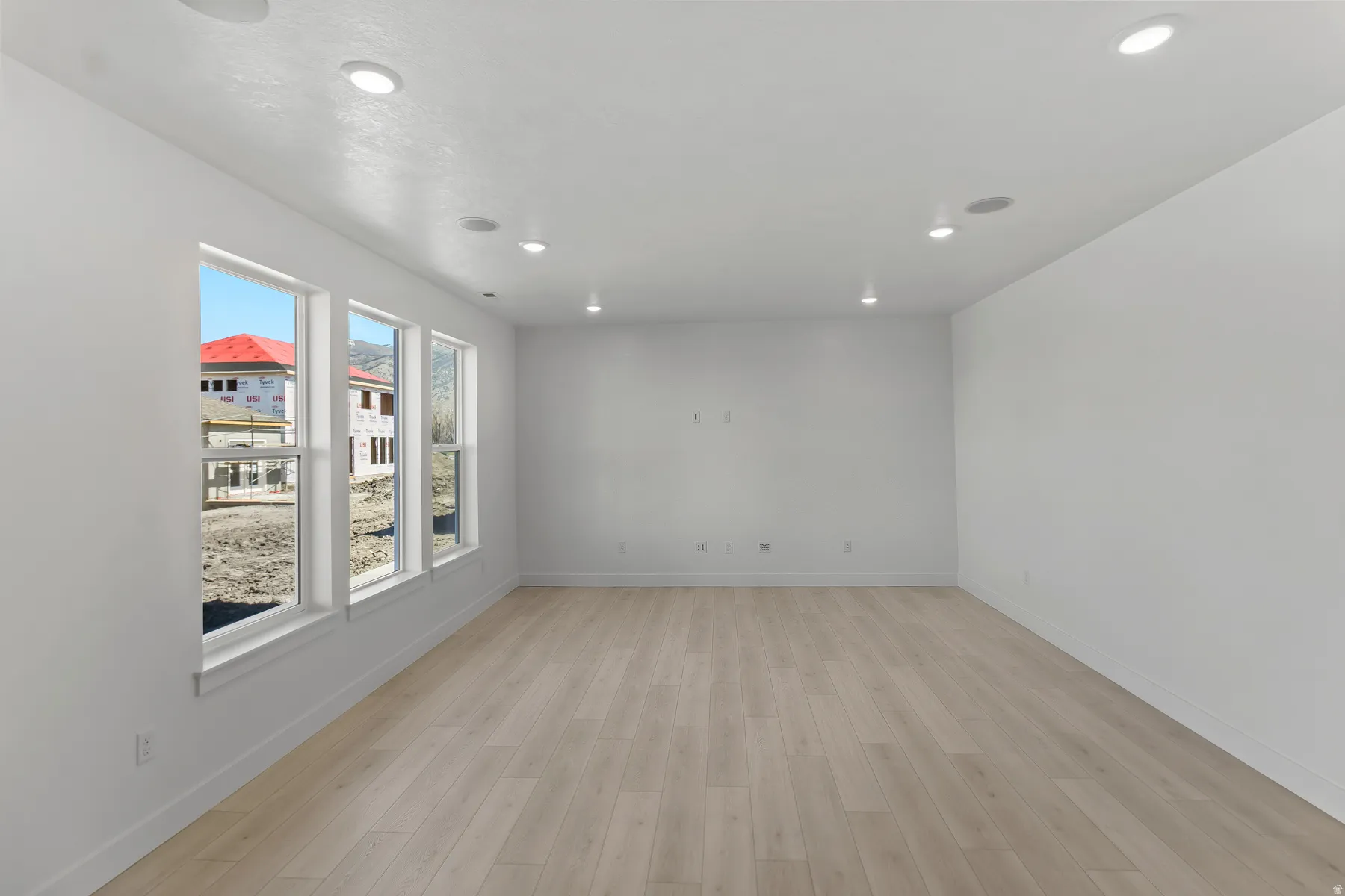 Spacious room featuring light wood-finish flooring, recessed lighting, and a series of three large windows providing abundant natural light
