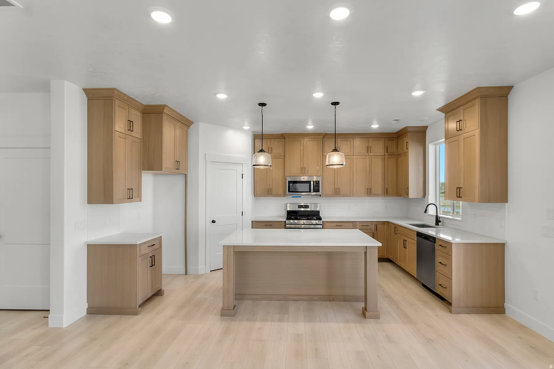 Bright kitchen featuring light wood-finish cabinetry, white countertops, and a subway tile backsplash