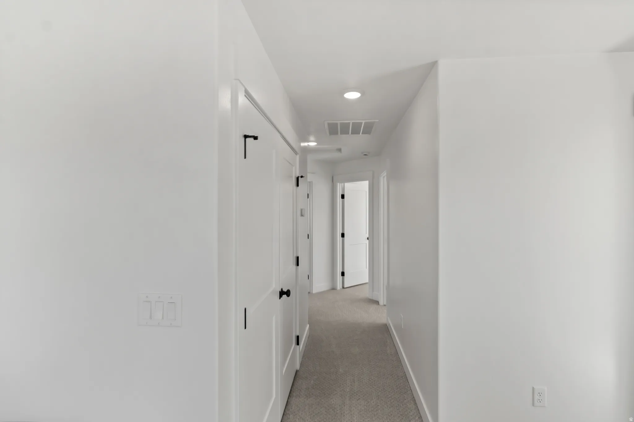 Hallway featuring recessed lighting, white paneled doors with matte black hardware, white walls, and light-toned carpet flooring