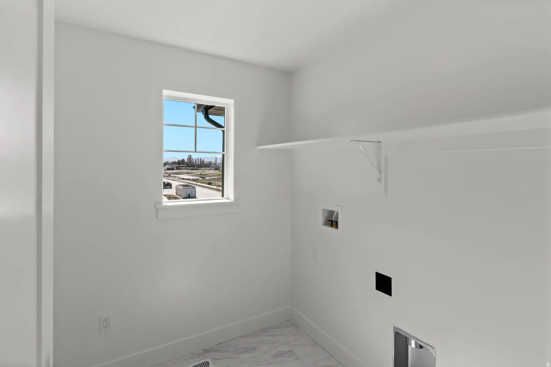 Dedicated utility room featuring a large window, overhead shelving, and marble-finish flooring