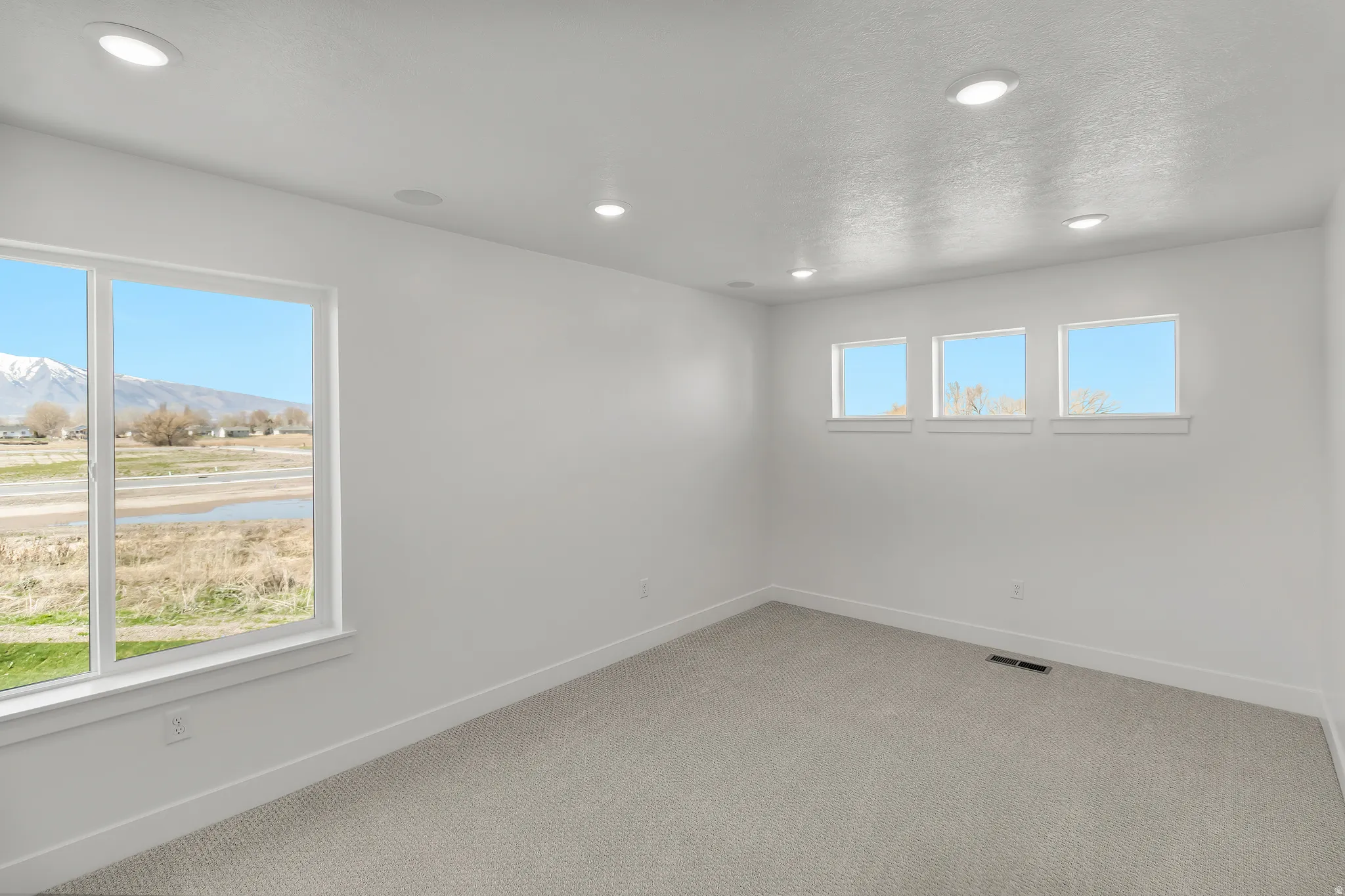 Spacious room with light gray carpeting, recessed ceiling lighting, and crisp white walls
