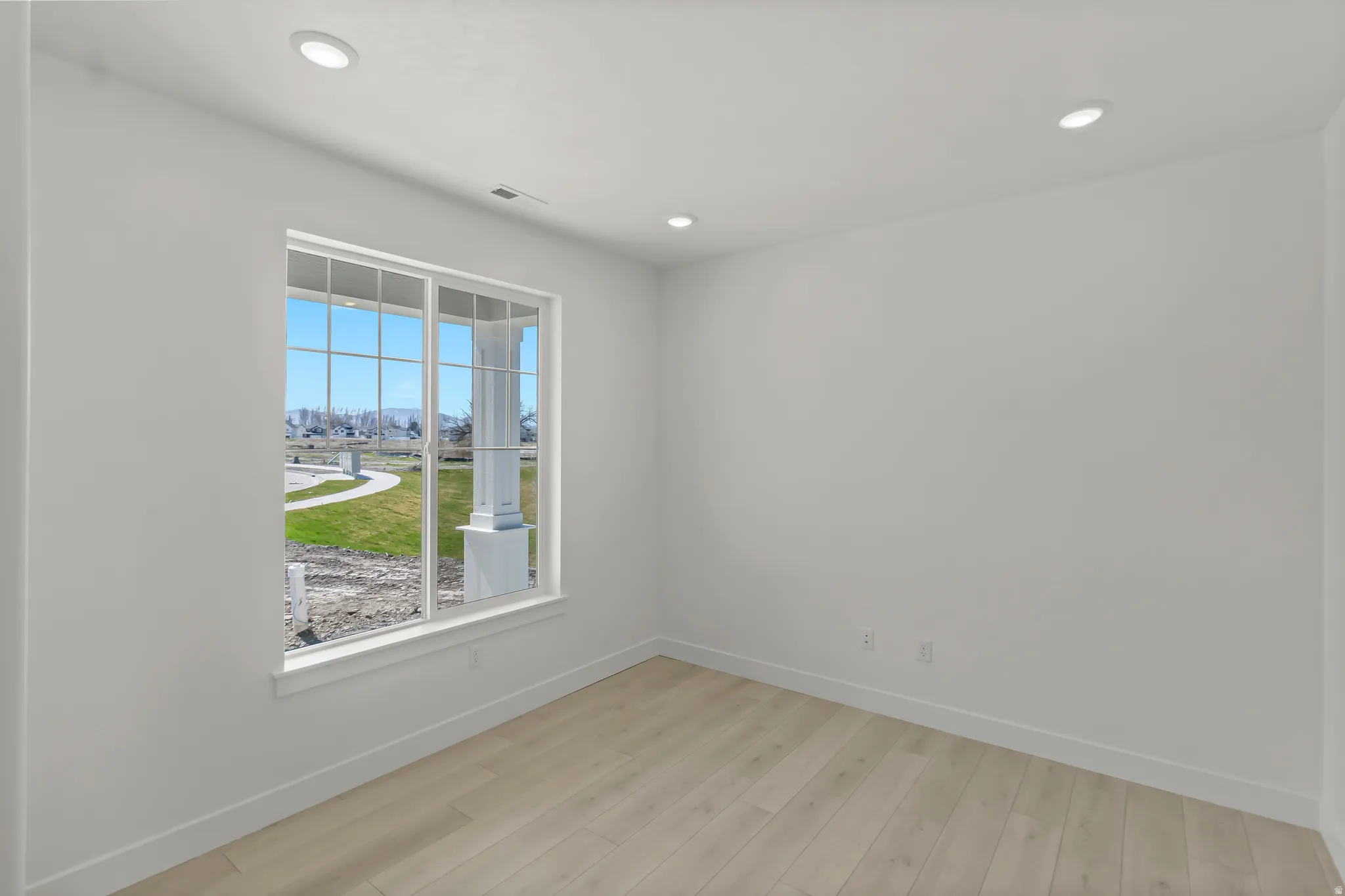 Bright room featuring a large multi-pane window, recessed lighting, light wood-finish flooring, white walls, and white baseboards