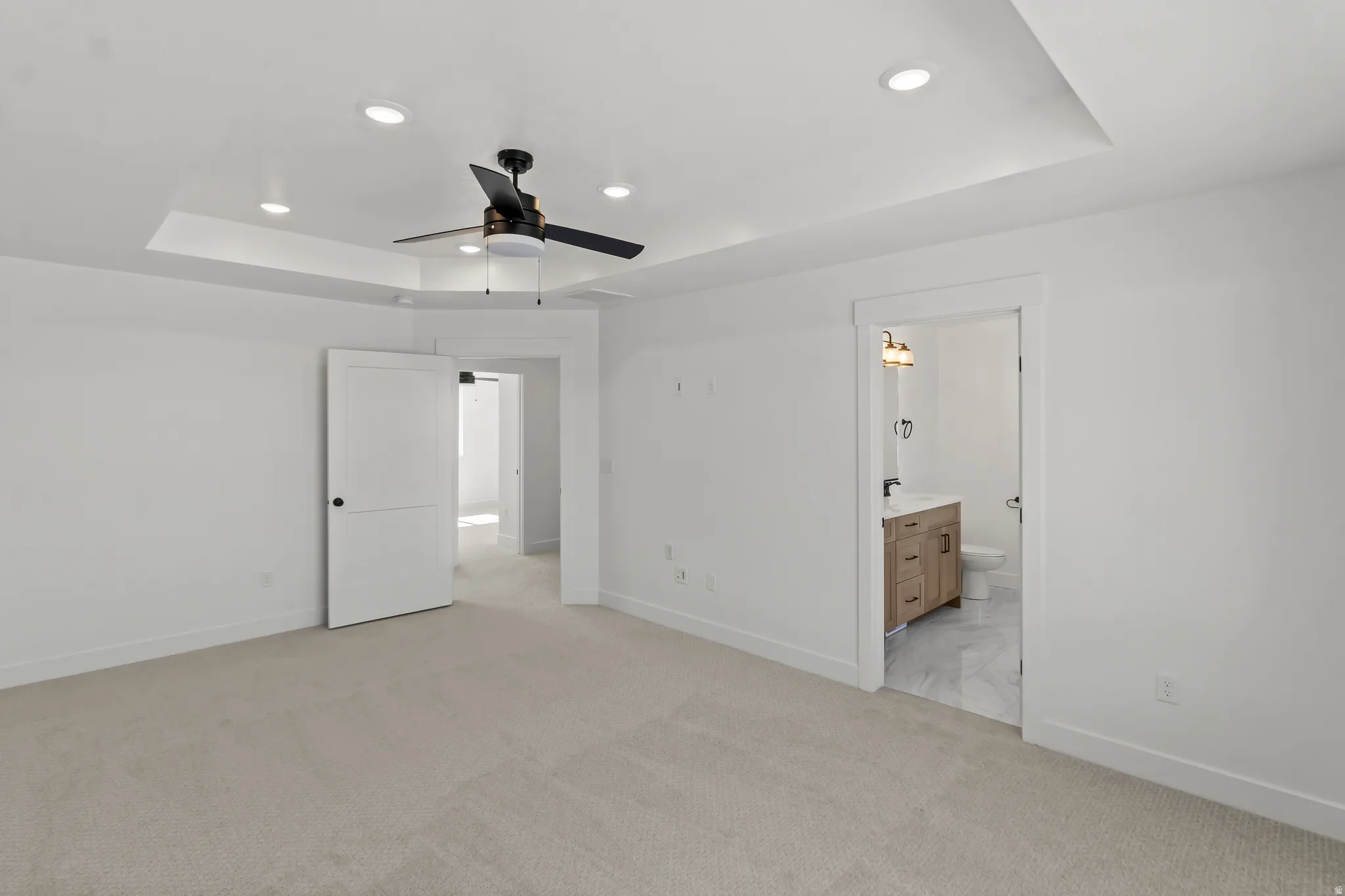 Spacious interior room featuring light-toned carpeting, a tray ceiling with recessed lighting, and a contemporary ceiling fan