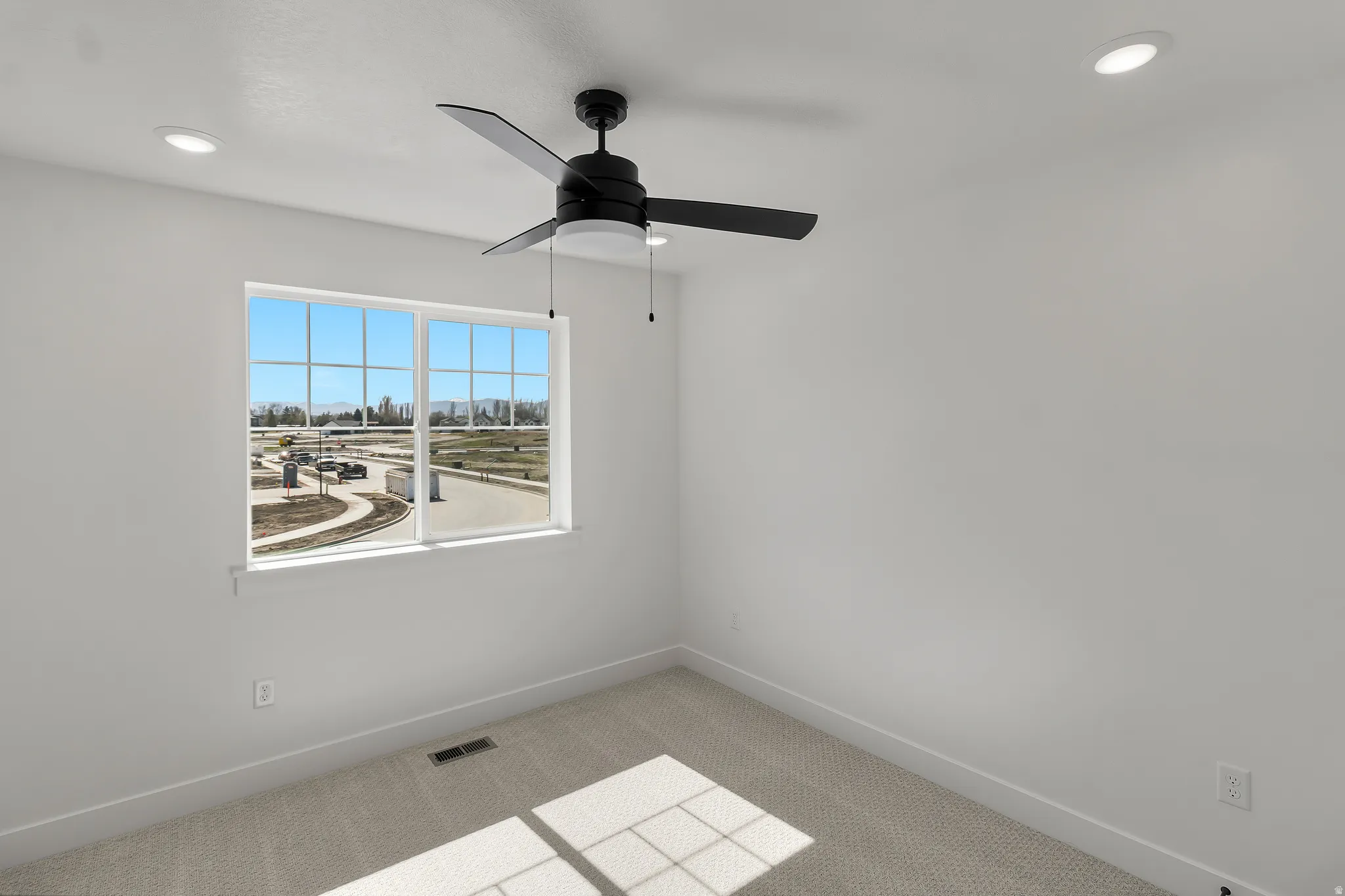Bright room featuring a large window, neutral carpeting, a contemporary black ceiling fan with light, recessed ceiling lighting, and white walls