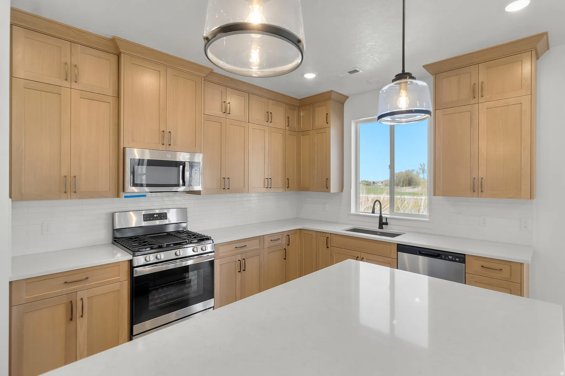 Modern kitchen featuring light wood-finish cabinetry, stainless steel appliances, white subway tile backsplash, and light countertops
