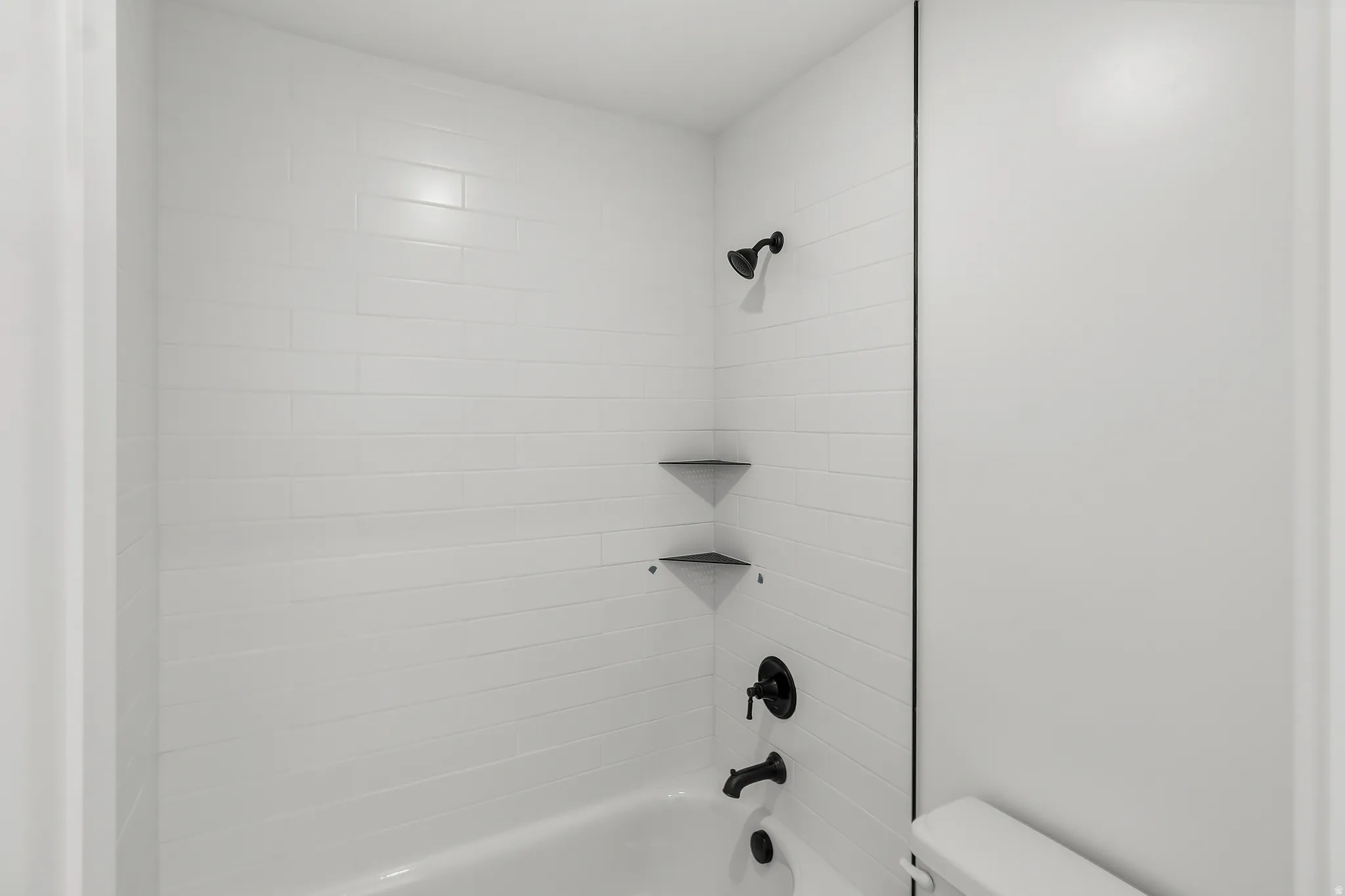 Bathtub with white subway tile surround, matte black shower fixtures, and integrated corner shelves