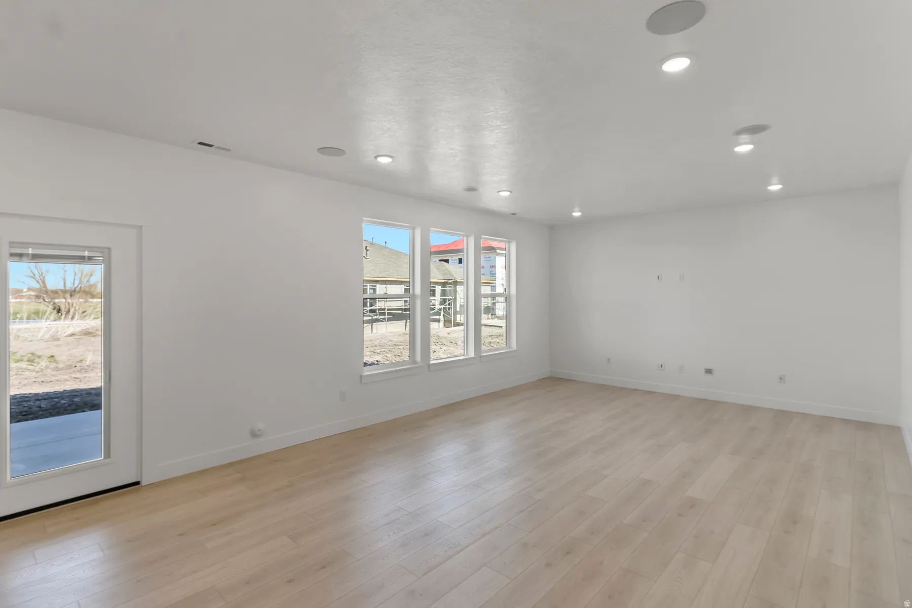 Spacious room featuring wood-finish flooring, white walls, multiple recessed lights, and a door with full-light glass paneling