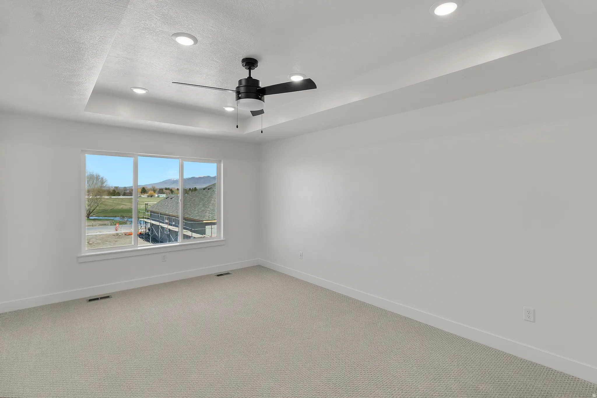 Spacious room featuring a tray ceiling with recessed lighting and a ceiling fan