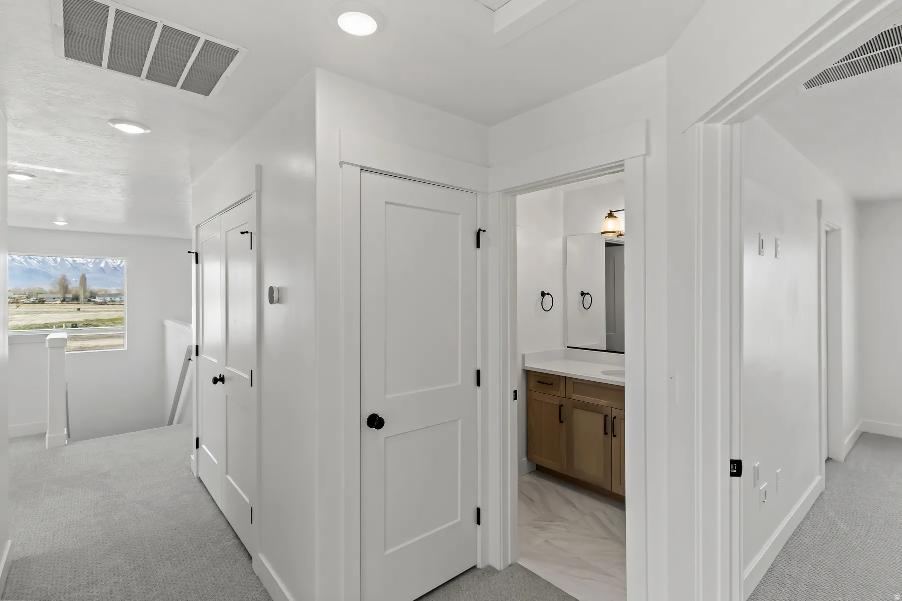 Hallway featuring light gray carpeting, white walls, recessed lighting, and a window with mountain scenery