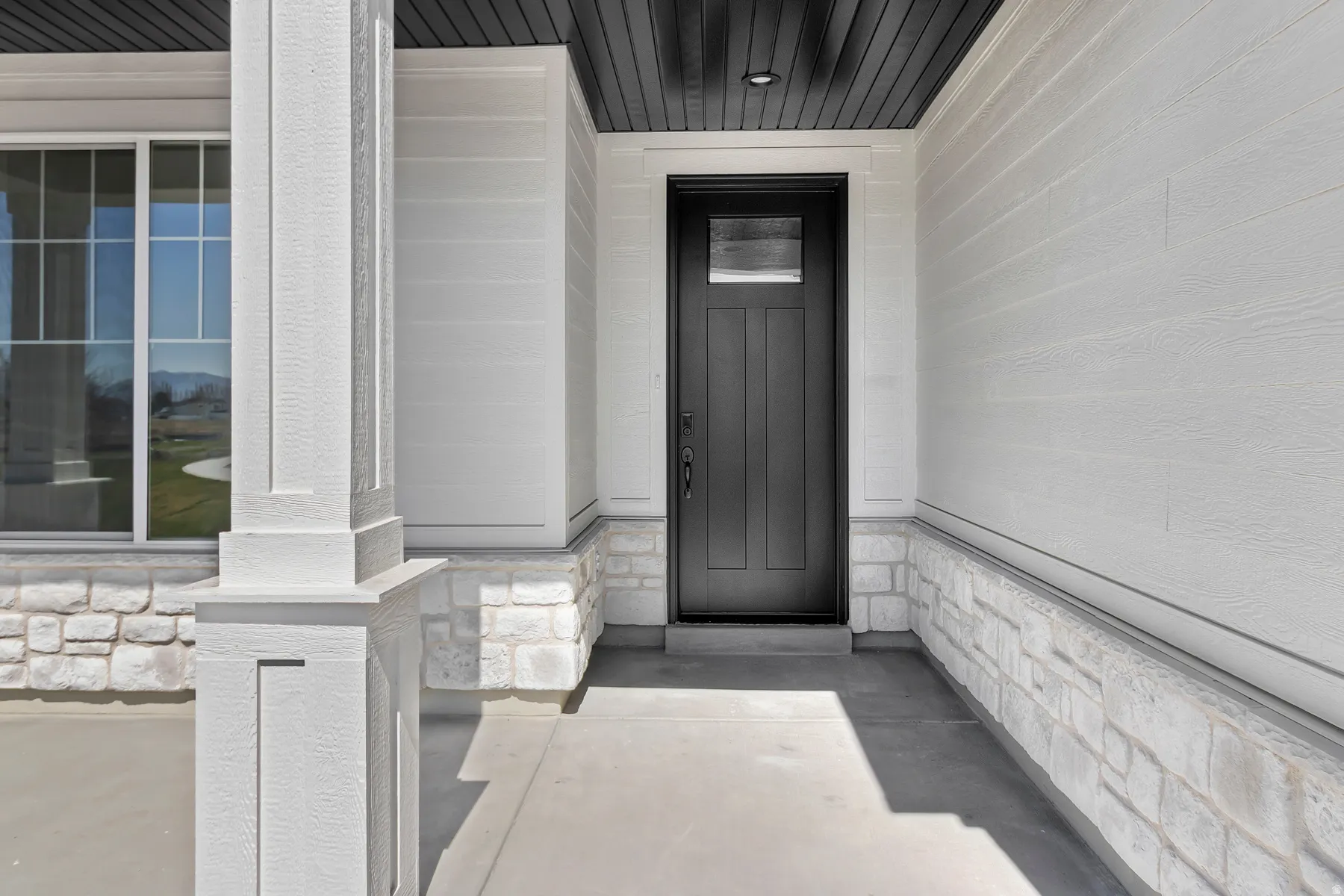 Entryway featuring a dark paneled door with glass insert, white horizontal siding, and a stone veneer foundation