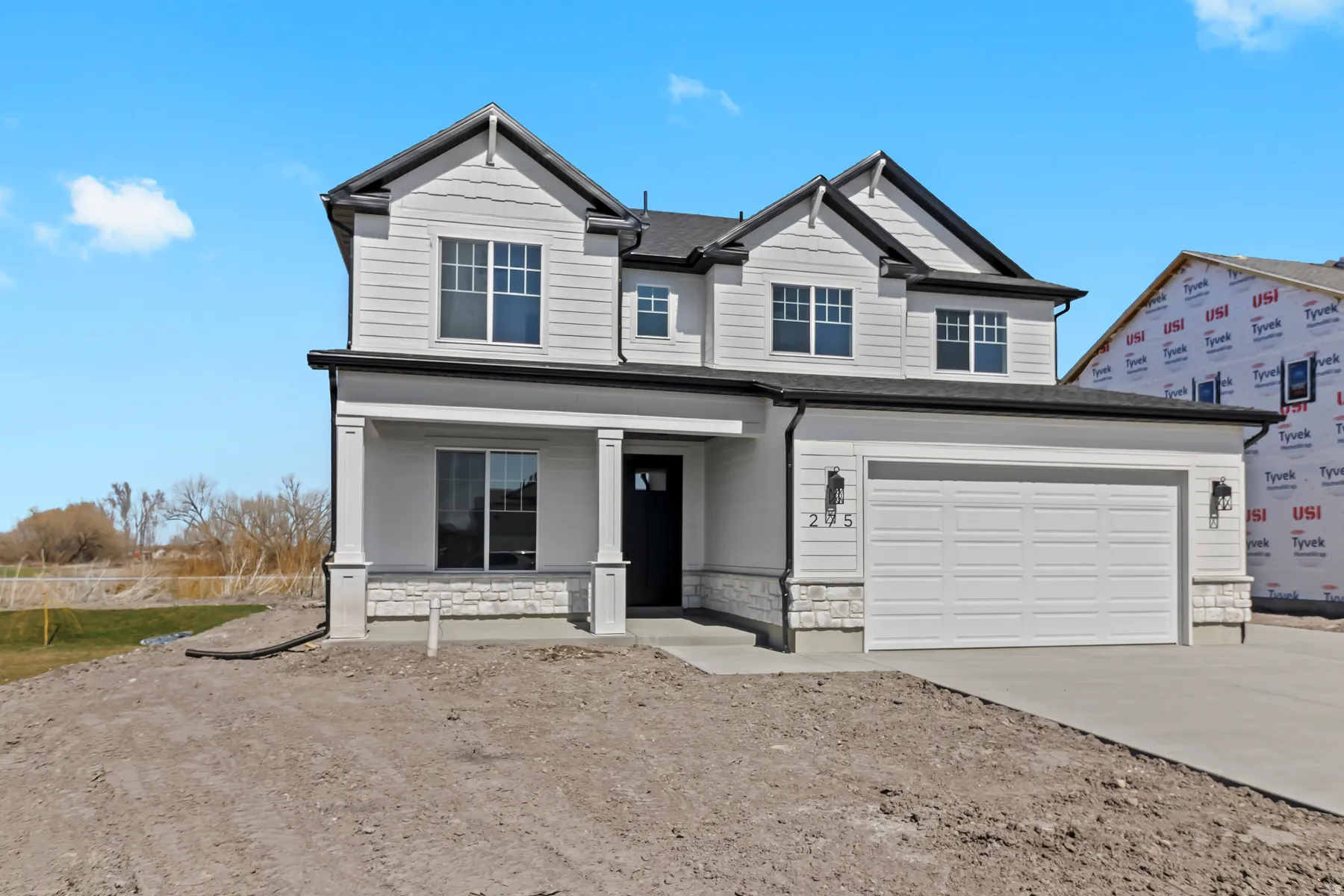 Two-story residence featuring white siding with dark trim accents, a prominent two-car garage, and a covered porch entry with stone detailing