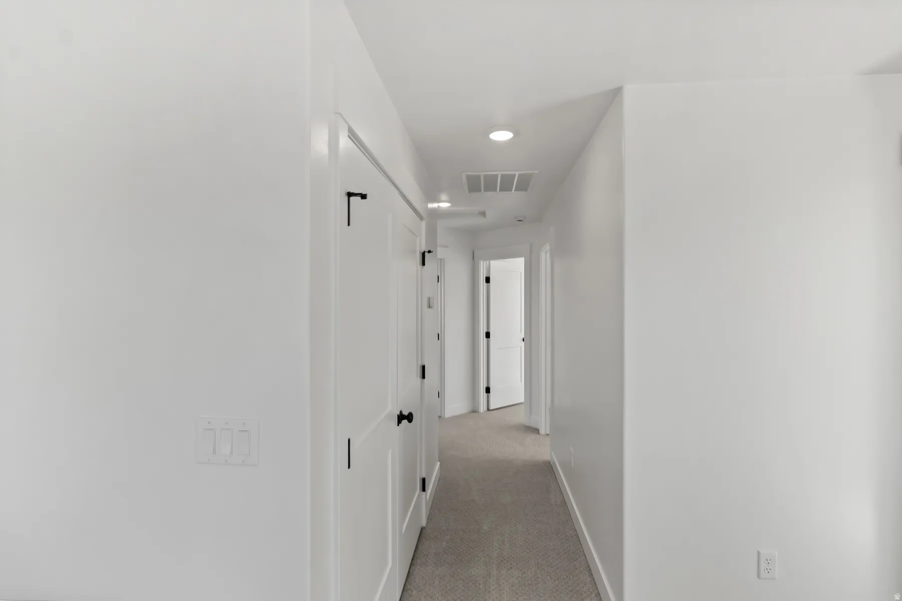 Interior hallway featuring recessed lighting, a neutral color palette, white doors with black hardware, and carpet flooring
