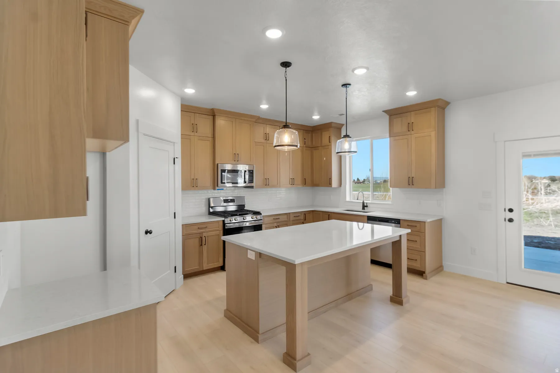 Kitchen featuring light wood-finish cabinetry, white subway tile backsplash, stainless steel appliances, and a central island with a white countertop