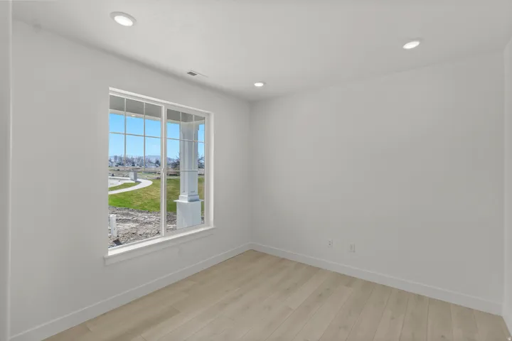 Bright room featuring a large multi-pane window, recessed lighting, light wood-finish flooring, white walls, and white baseboards