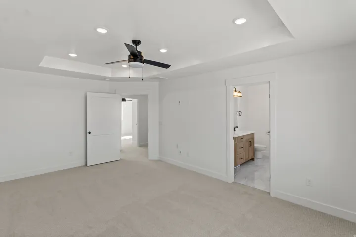 Spacious interior room featuring light-toned carpeting, a tray ceiling with recessed lighting, and a contemporary ceiling fan