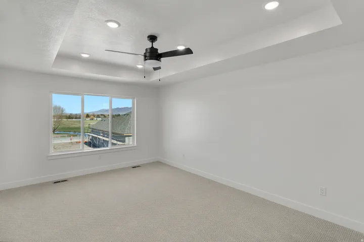 Spacious room featuring a tray ceiling with recessed lighting, a modern ceiling fan, large windows, and neutral carpeting