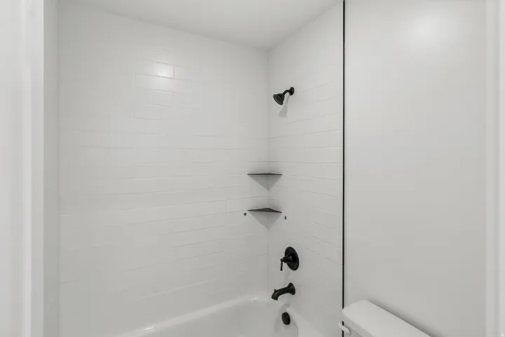 Bathtub with white subway tile surround, matte black shower fixtures, and integrated corner shelves