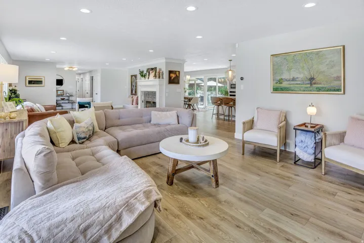 Open-concept living area featuring wood-finish flooring, recessed lighting, and a white fireplace surround
