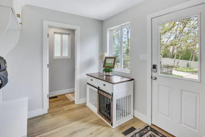 Entryway featuring a white paneled door with a glass insert, wood-finish flooring, light grey walls, and a built-in white storage bench with brass hardware