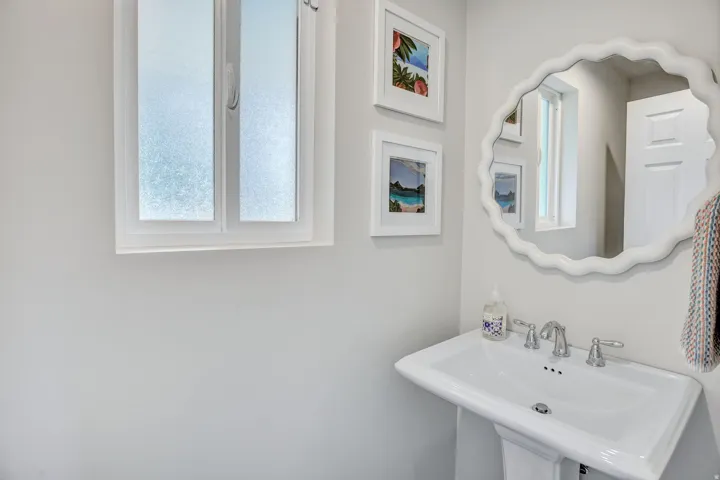 Pedestal sink with chrome-finish faucet and white scalloped mirror
