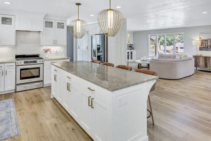 Kitchen featuring a large center island with a stone countertop, white shaker cabinetry with brass hardware, and wood-finish flooring