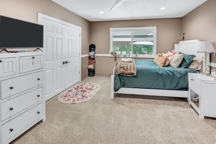Carpeted room with neutral-toned walls, featuring a window with exterior views, white paneled double doors, recessed lighting, and a ceiling fan