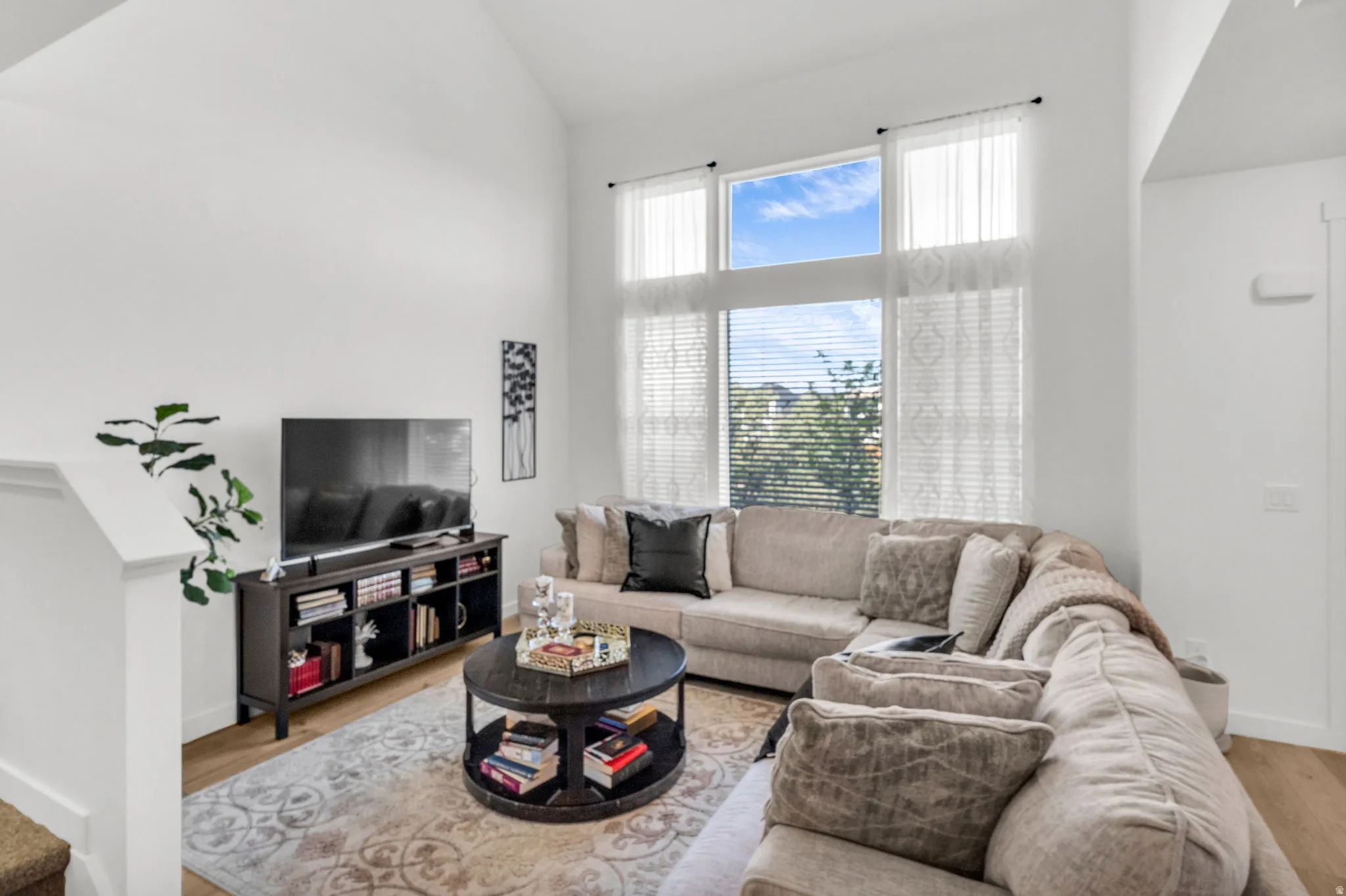 Living area featuring high vaulted ceilings, expansive window wall with transoms, and light wood-finish flooring