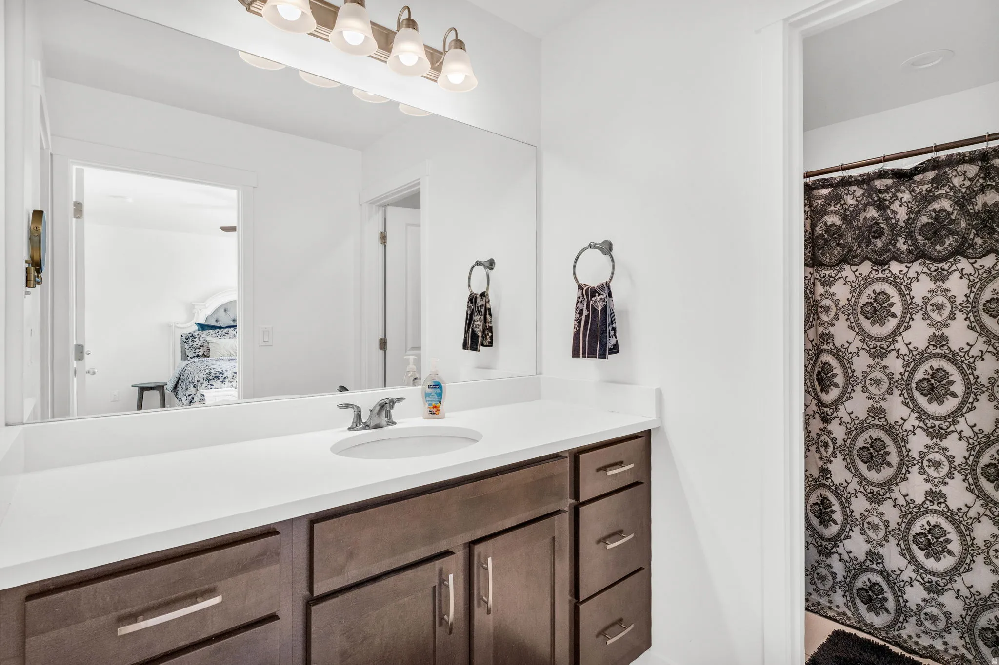 Bathroom featuring a single vanity with a large mirror, a white countertop, and dark wood-finish cabinetry with brushed nickel hardware