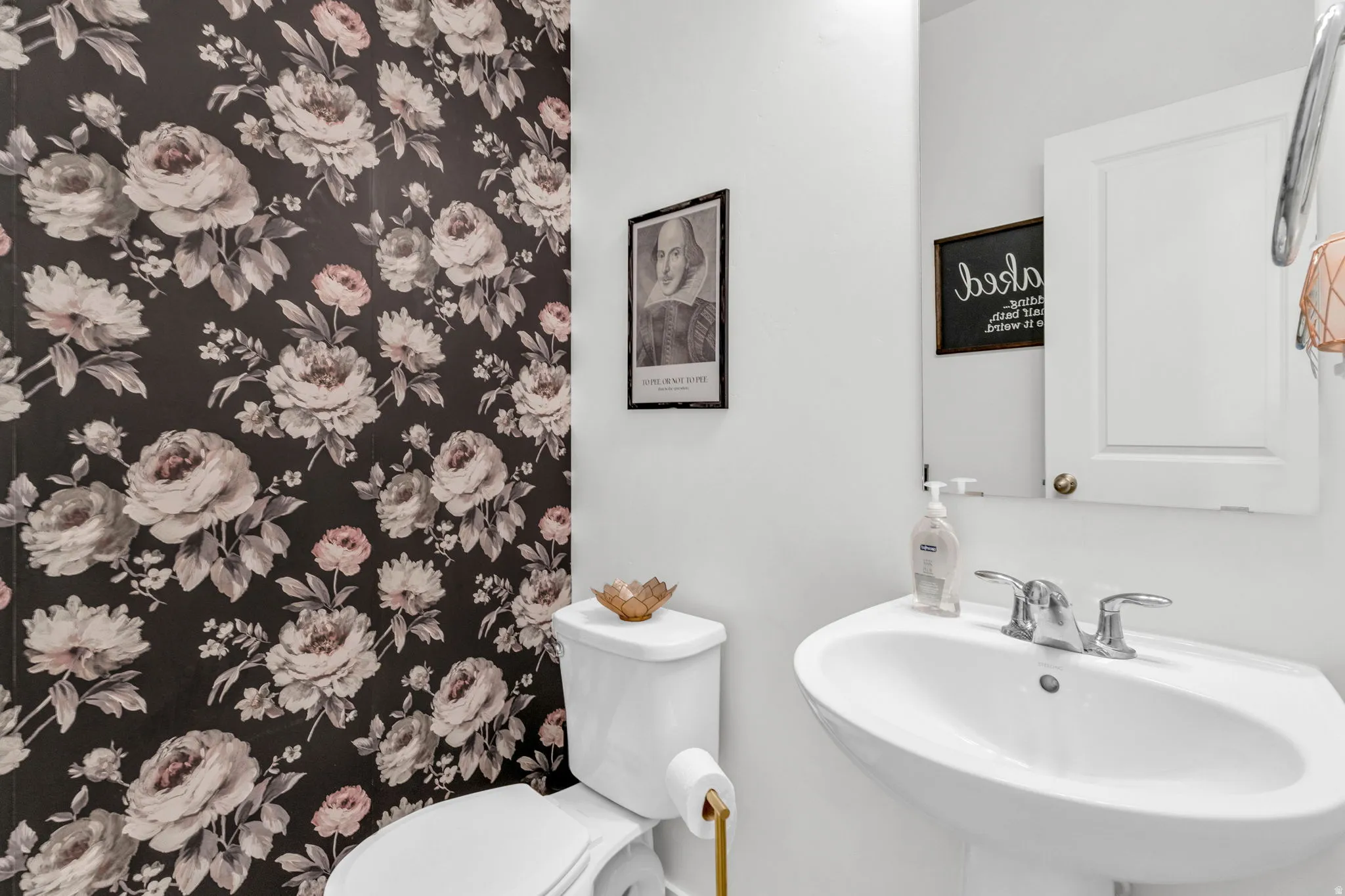 Powder room featuring a floral accent wall with dark background, pedestal sink, and a two-piece toilet