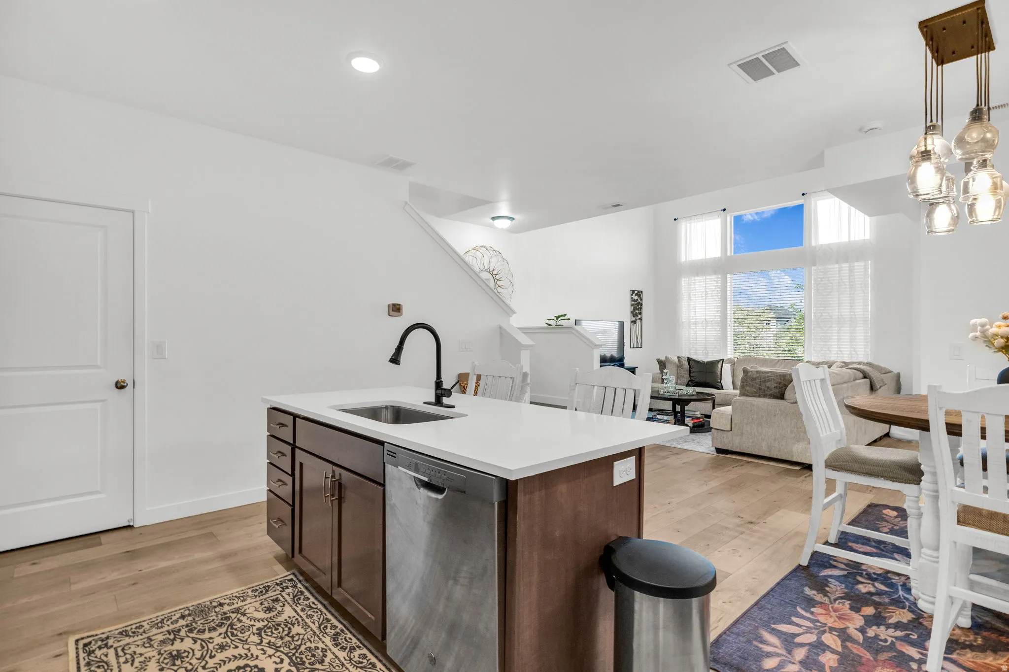 Kitchen island featuring a stainless steel sink with a gooseneck faucet, light-colored countertop, and dark wood-finish cabinetry