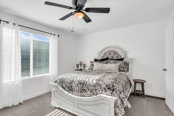 Bedroom featuring light gray carpeting, crisp white walls, a large window with blinds, and a black ceiling fan with an integrated light fixture