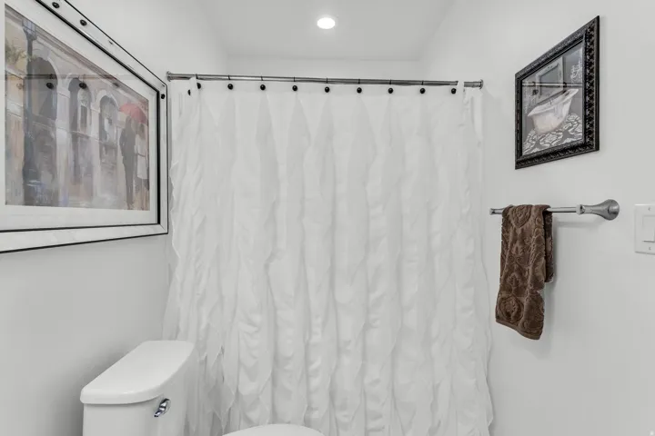 Compact bathroom featuring a white toilet, recessed lighting, white walls, and a shower with a textured white curtain