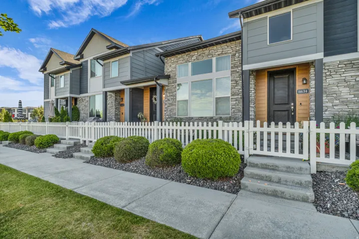 Modern townhome exterior featuring multi-toned siding, stone accents, and a crisp white picket fence