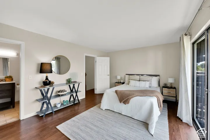 Spacious Primary bedroom featuring wood-finish flooring, light neutral wall tones, and an open doorway to an adjacent bathroom with a vanity