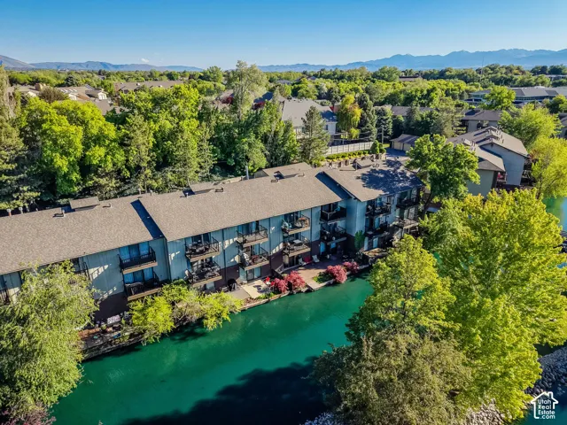 Waterfront multi-story residence featuring individual balconies, mature surrounding trees, and a clear blue sky