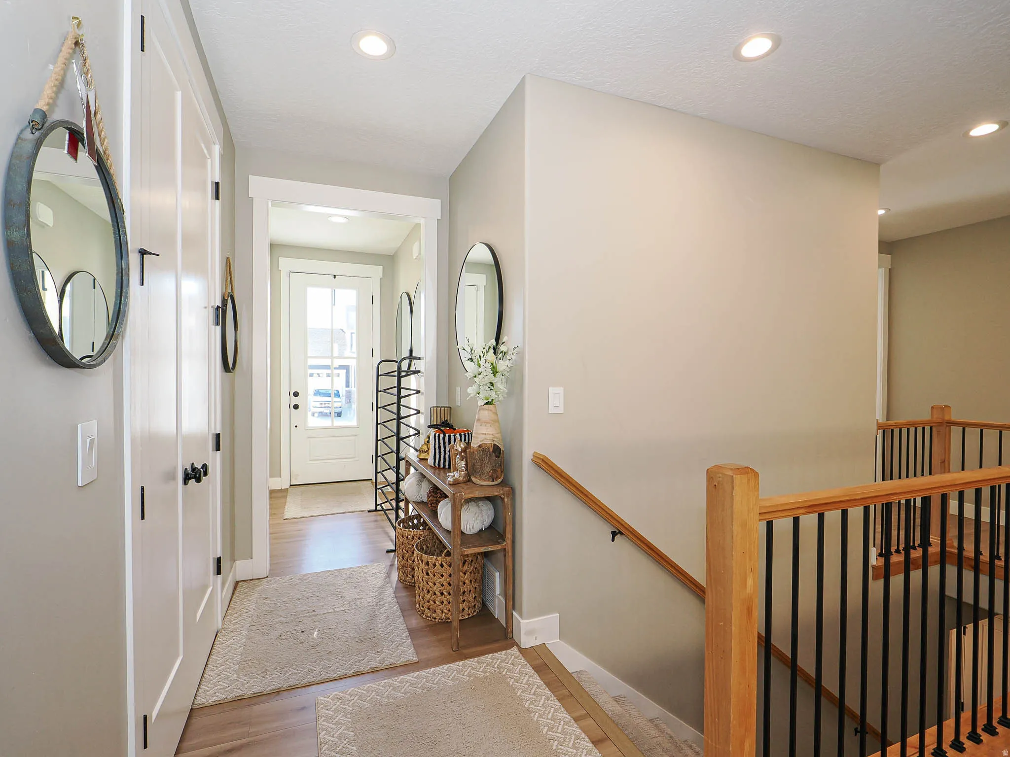 Entryway and staircase featuring wood-finish flooring, recessed lighting, white doors with black hardware, and a staircase with wood newel posts and black metal balusters