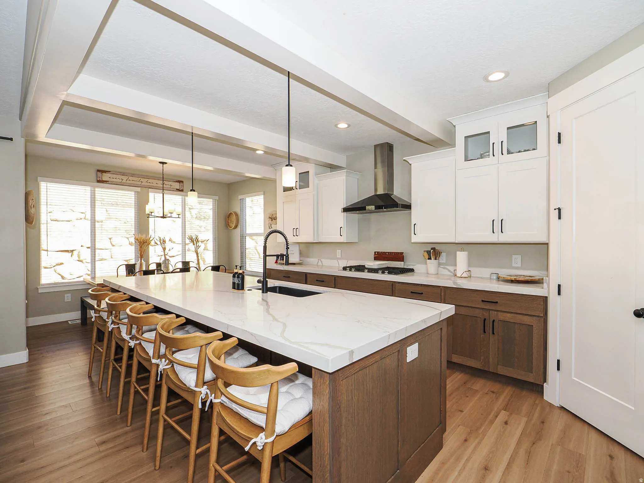 Spacious kitchen featuring a large central island with seating, wood-finish flooring, two-tone cabinetry, stainless steel range hood, and a recessed tray ceiling
