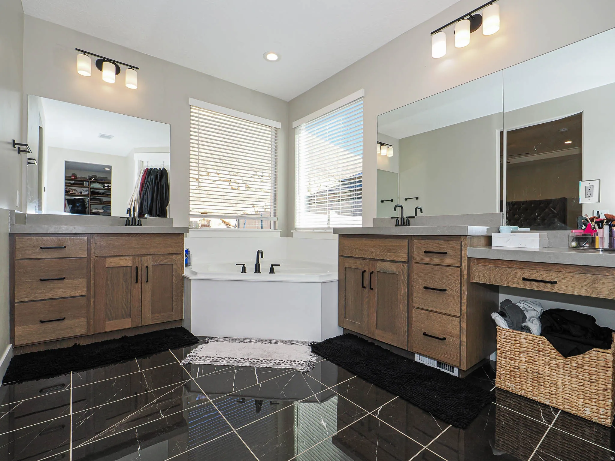 Bathroom featuring dual wood-finish vanities with light-toned countertops, black hardware, and large mirrors