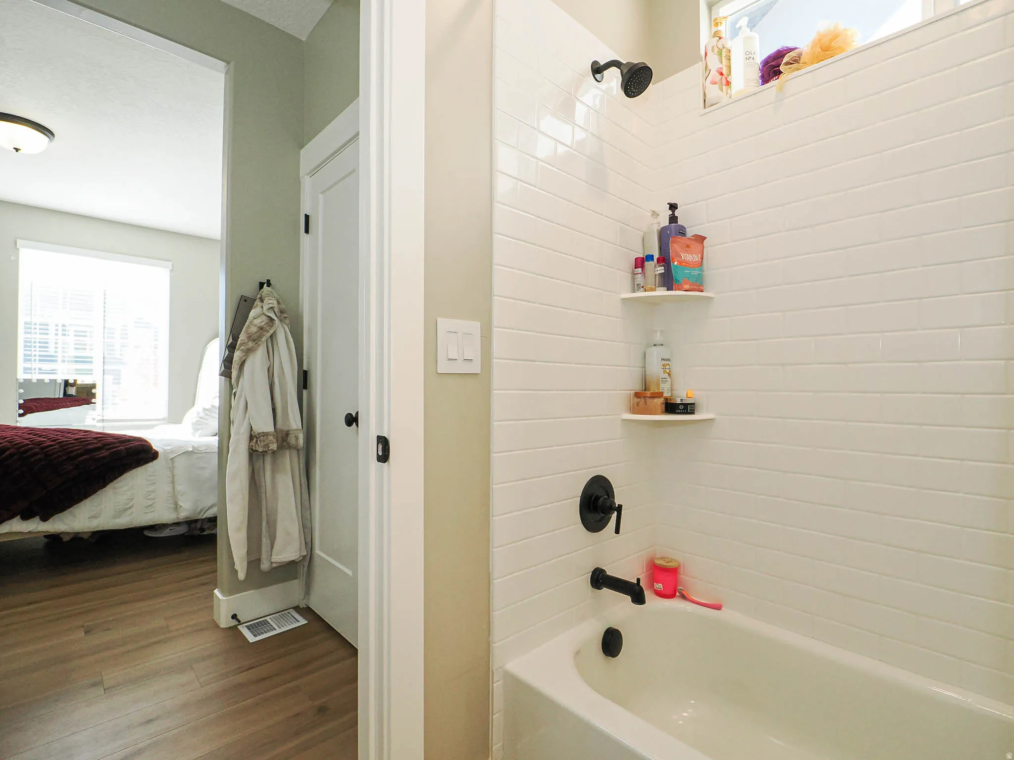 Bathtub with white subway tile surround, matte black fixtures, and built-in corner shelving