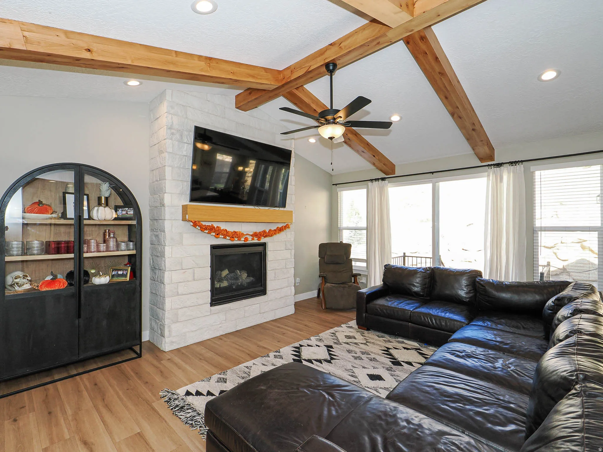 Living area featuring a floor-to-ceiling brick fireplace with a wood mantle, vaulted ceiling with exposed wood beams, recessed lighting, and wood-finish flooring