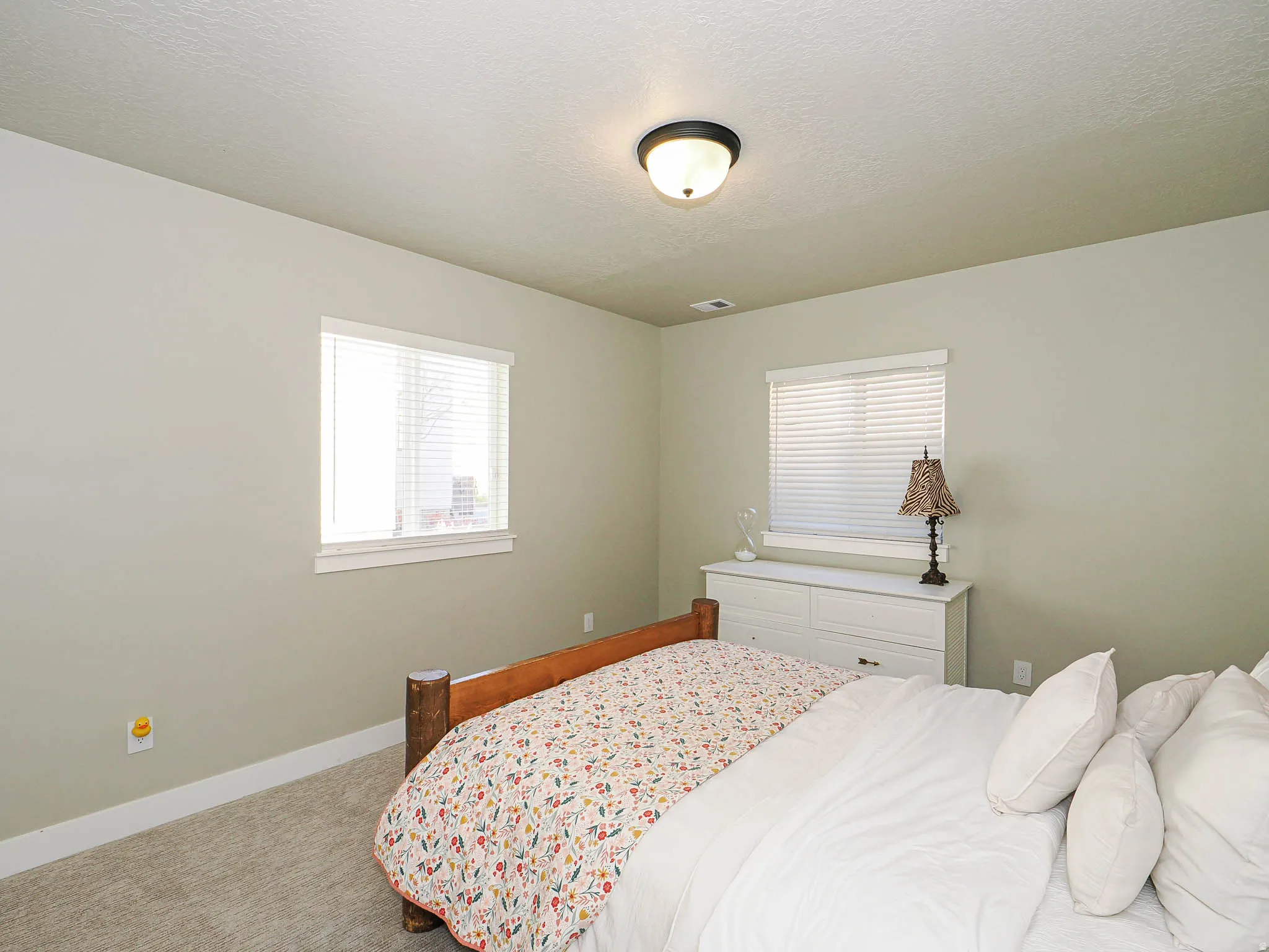 Bedroom featuring two windows with horizontal blinds, light-toned wall paint, and a ceiling-mounted light fixture