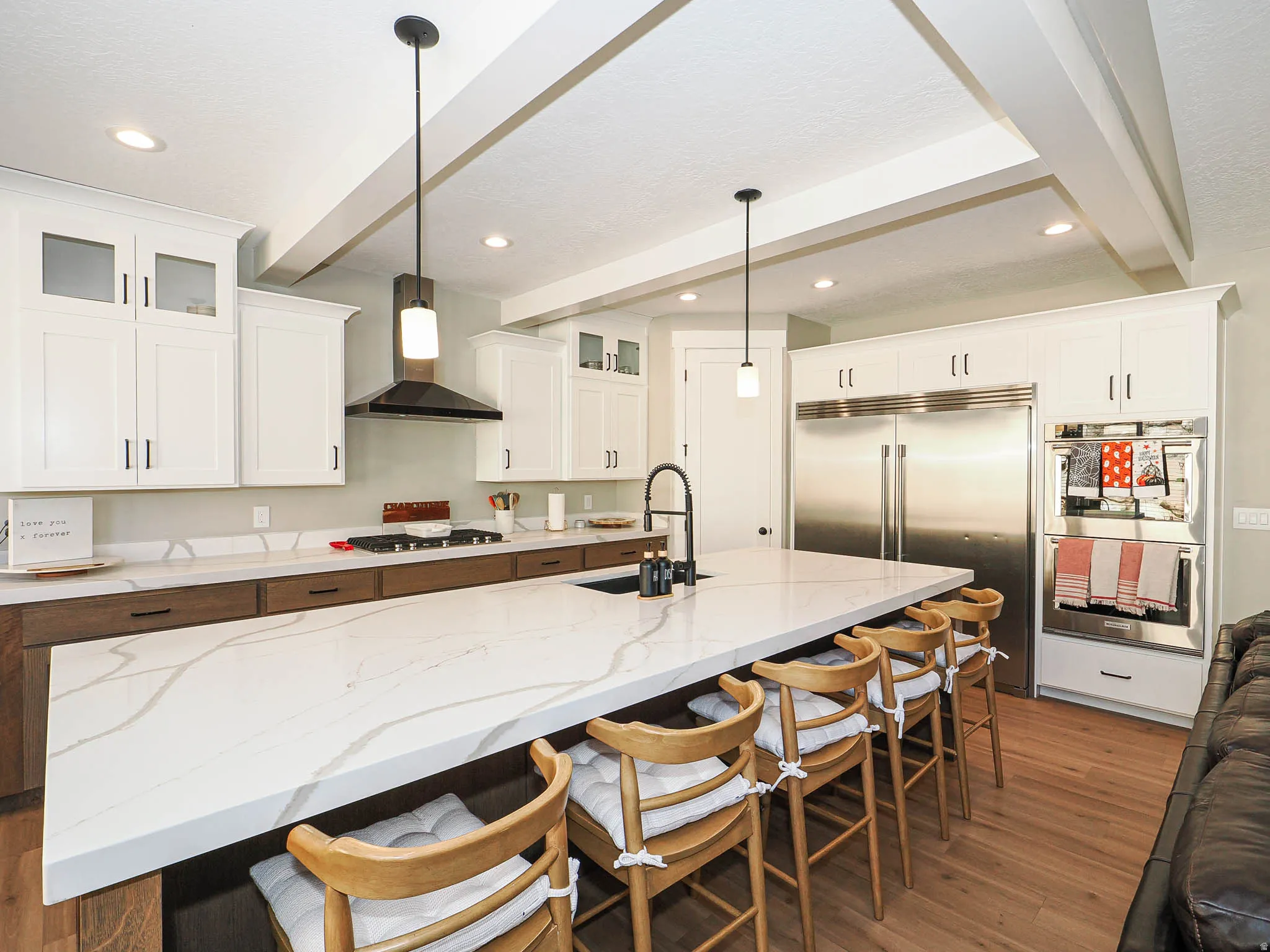 Open-concept kitchen featuring an expansive island with a waterfall edge, white shaker cabinetry, stainless steel appliances, and wood-finish flooring