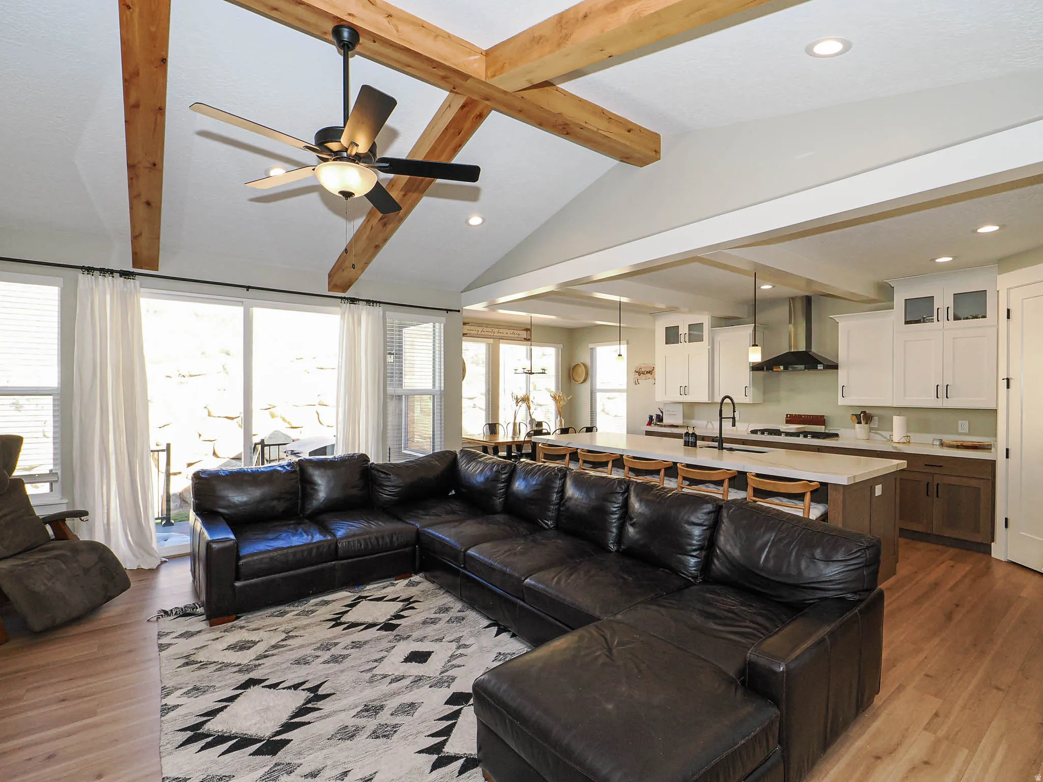 Open-concept living area featuring vaulted ceilings with exposed wood beams, a ceiling fan, and recessed lighting
