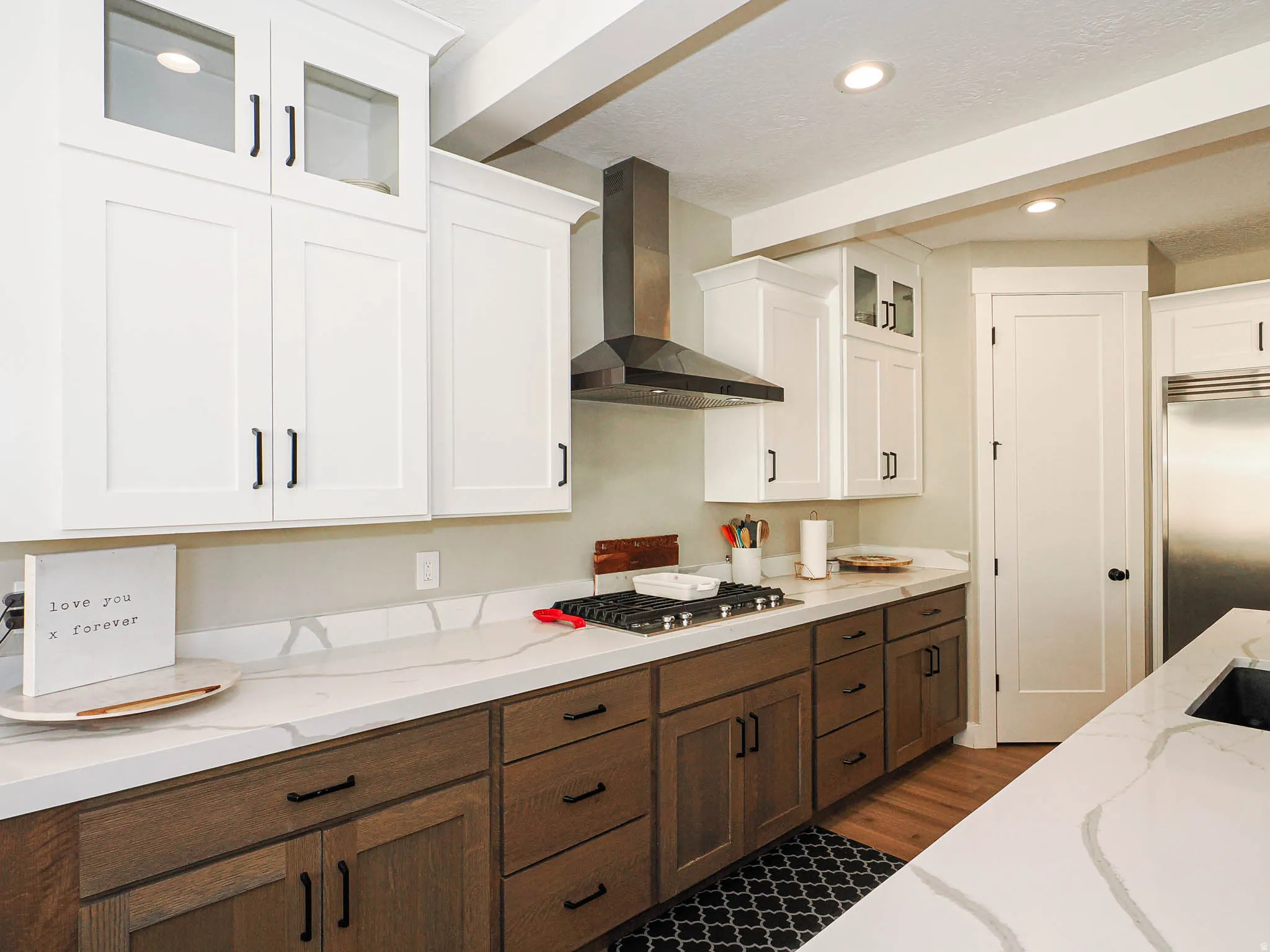 Modern kitchen featuring white upper cabinetry with glass inserts, wood-finish lower cabinetry, and extensive light-toned countertops with veining