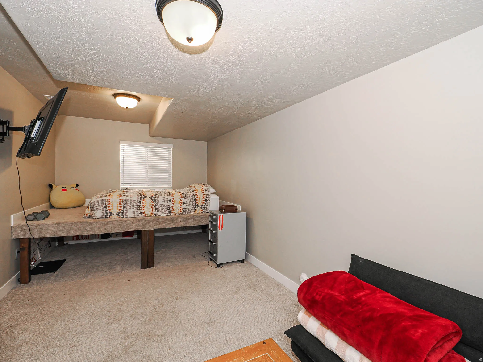 Carpeted bedroom featuring a built-in platform bed, a wall-mounted television, and a window with blinds