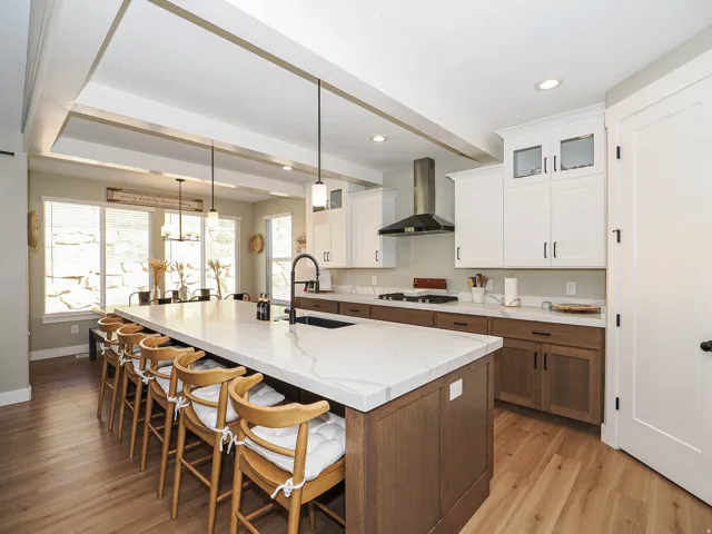 Spacious kitchen featuring a large central island with seating, wood-finish flooring, two-tone cabinetry, stainless steel range hood, and a recessed tray ceiling
