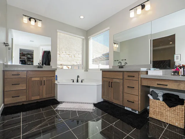 Bathroom featuring dual wood-finish vanities with light-toned countertops, black hardware, and large mirrors