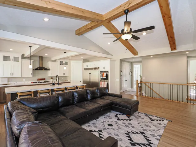 Vaulted ceiling with exposed wood beams and ceiling fan, wood-finish flooring, white cabinetry, a kitchen island with seating, and stainless steel appliances