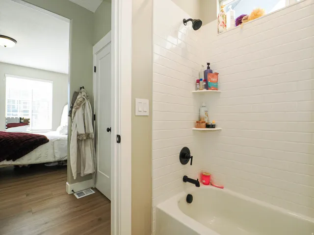 Bathtub with white subway tile surround, matte black fixtures, and built-in corner shelving